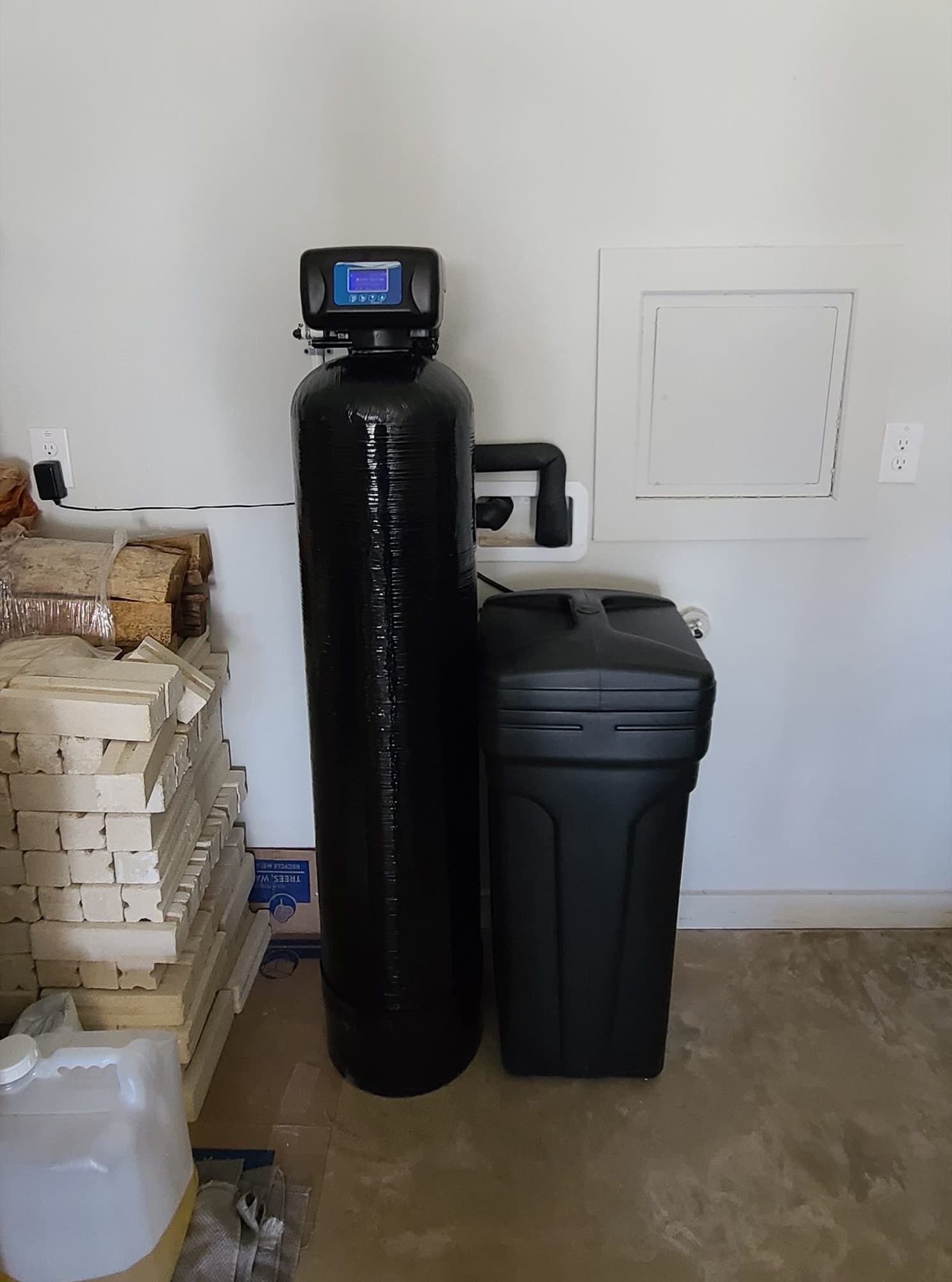 Water softener and brine tank installed next to a stack of leftover bricks